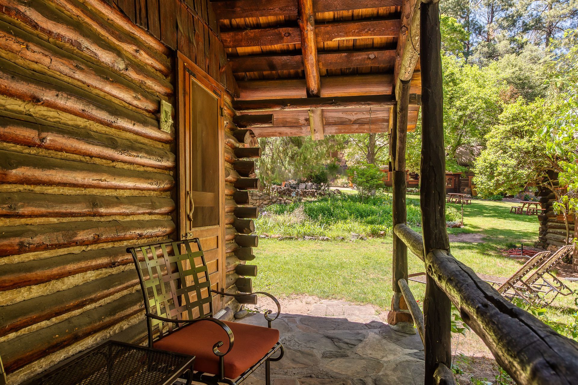 Covered porch of a log cabin with a chair, overlooking a grassy yard and trees.