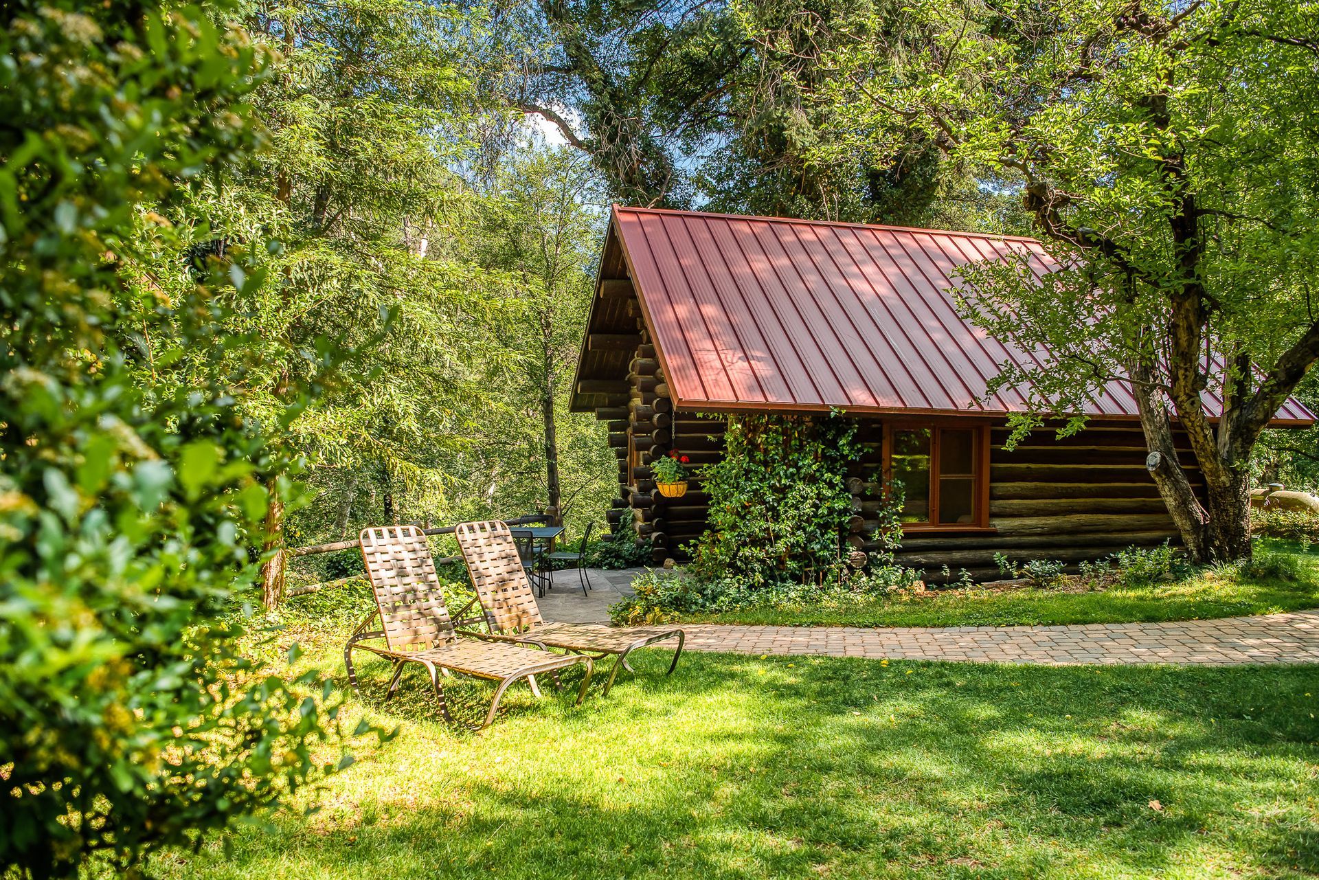 Log cabin nestled in lush greenery with lawn chairs.