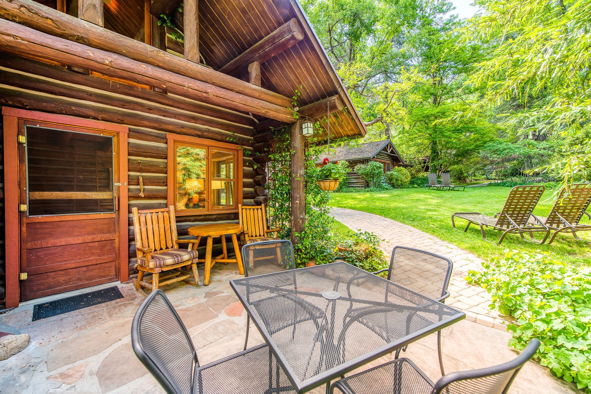 A cozy cabin with a patio set, wooden chairs, and a lush green yard.