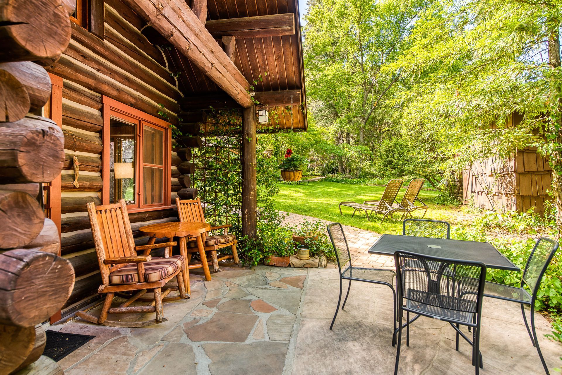 Log cabin porch with seating; sunny backyard with trees.