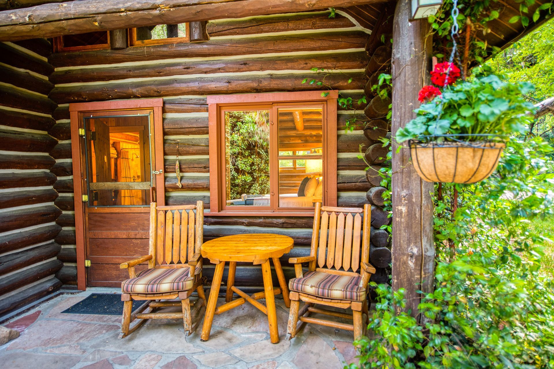 Wooden cabin porch with chairs, table, hanging plants; inviting outdoor seating.