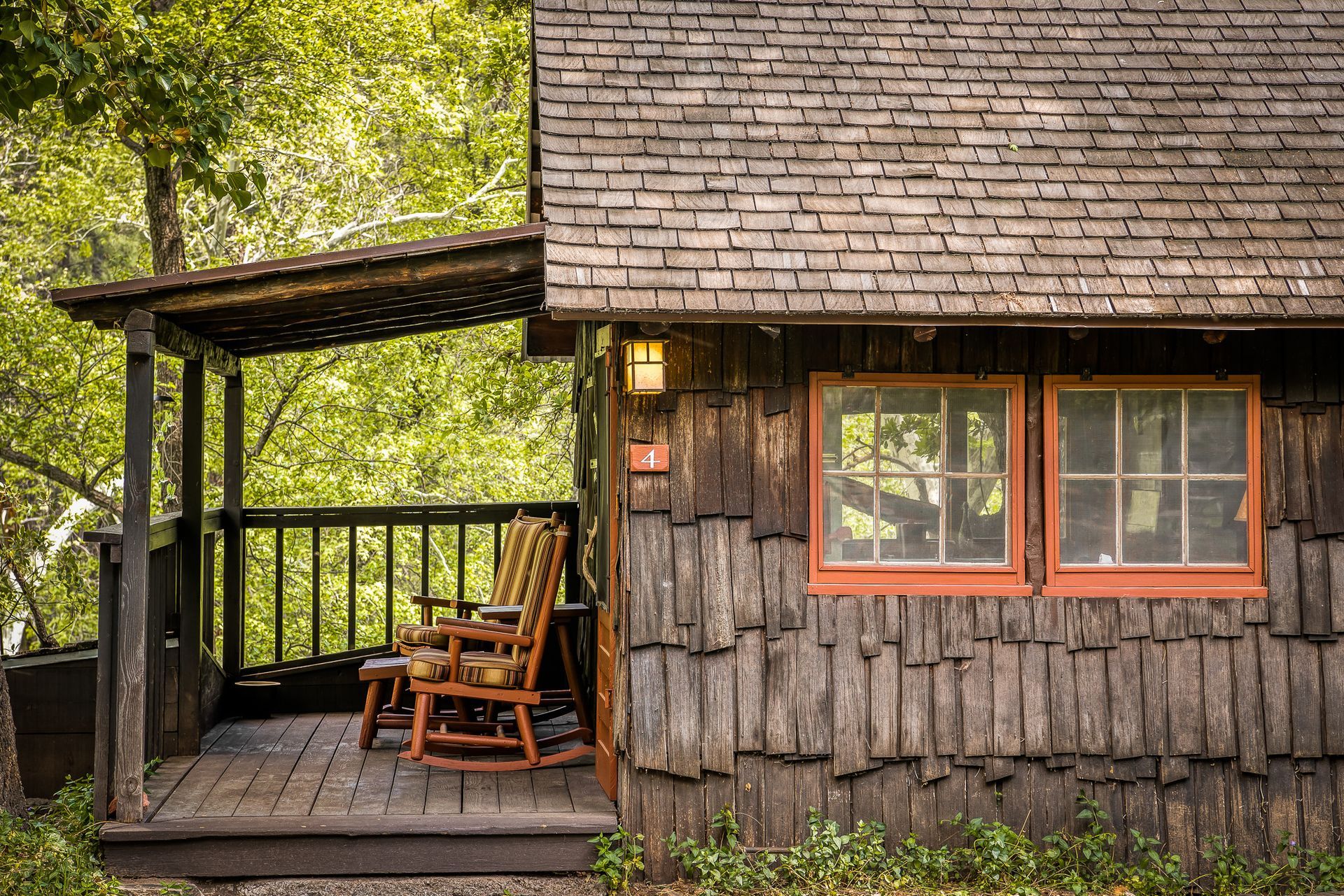 Wooden cabin with porch and two rocking chairs, windows with orange trim.