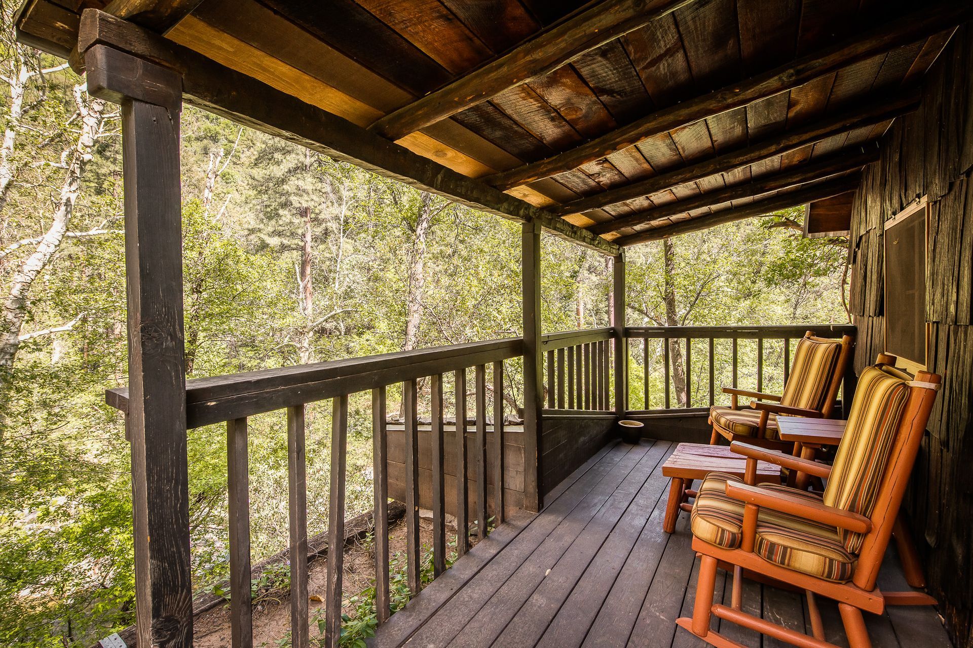 Wooden cabin porch with rocking chairs, overlooking a green forest.