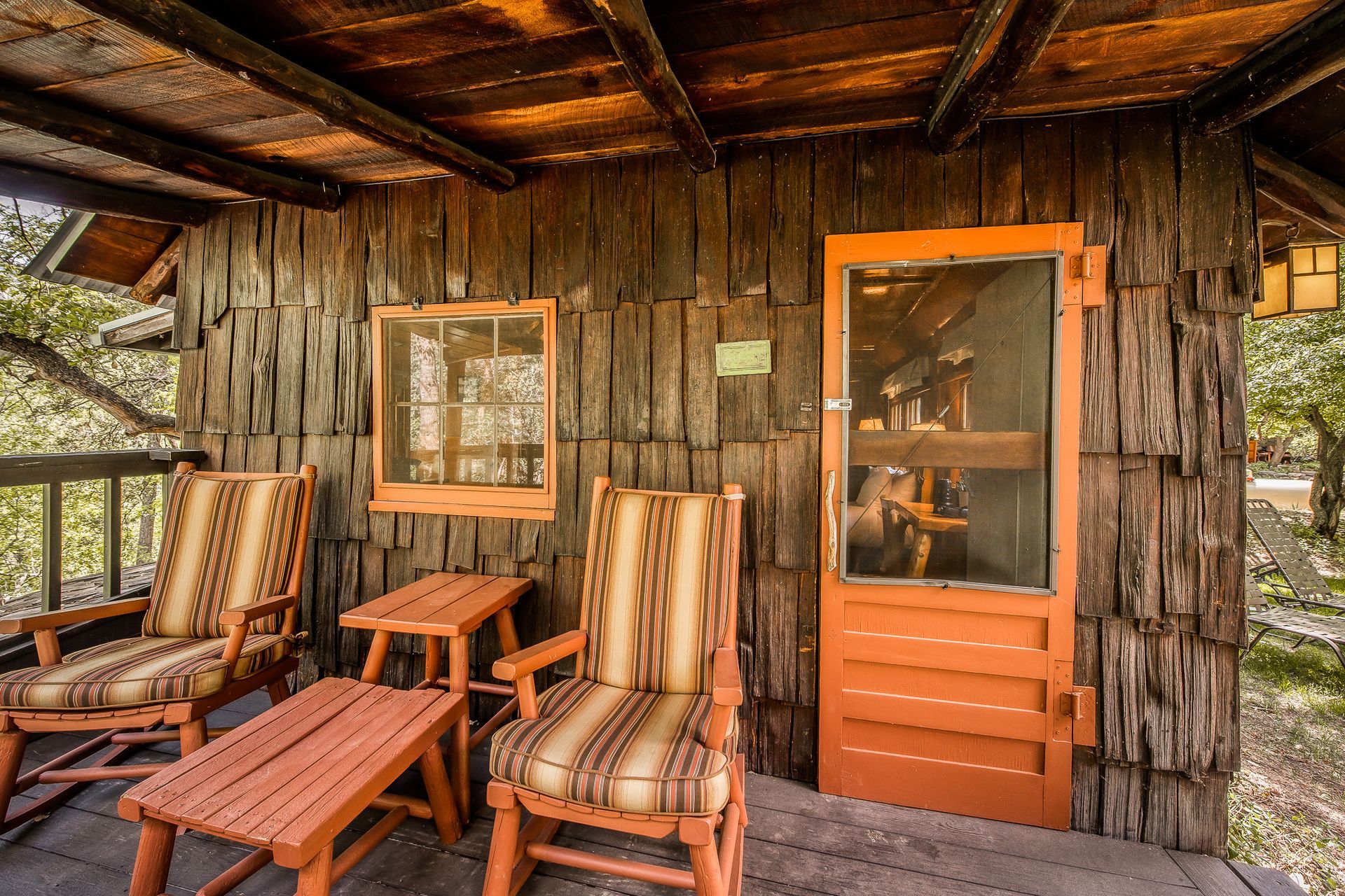 Rustic porch with two striped chairs, small table, screen door.