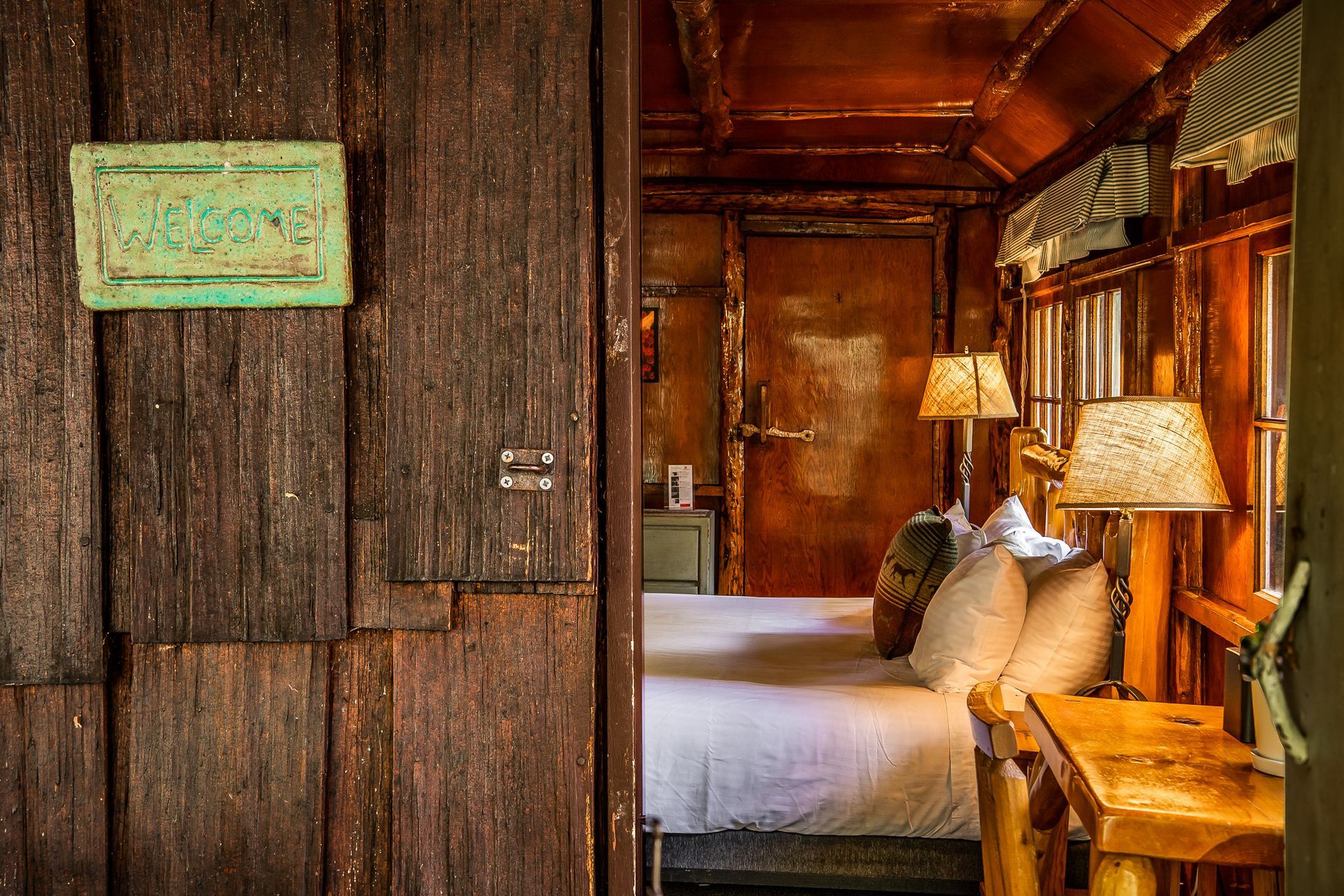 Rustic bedroom interior with wooden walls, a bed, and lamps.
