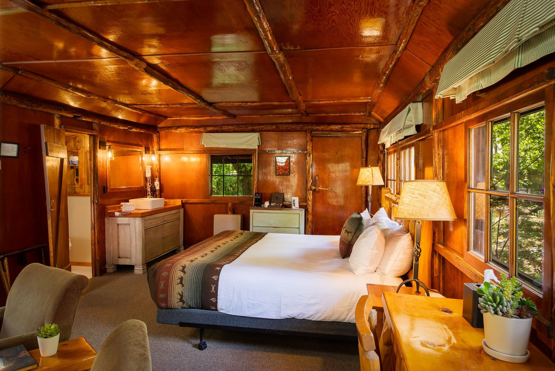 Cozy hotel room with a bed, desk, and windows; wooden interior.