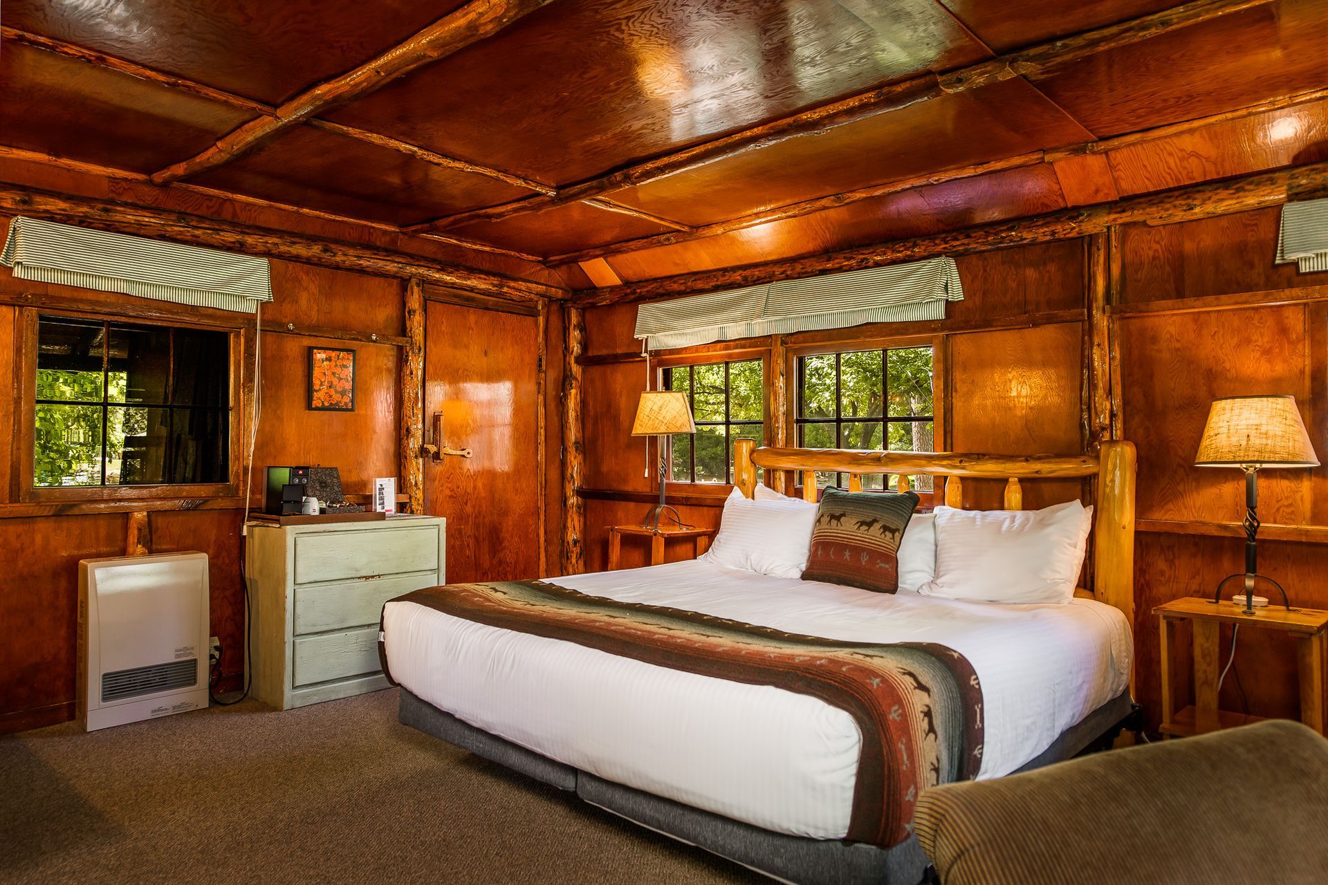 Rustic cabin bedroom with wooden walls, a large bed, and windows.