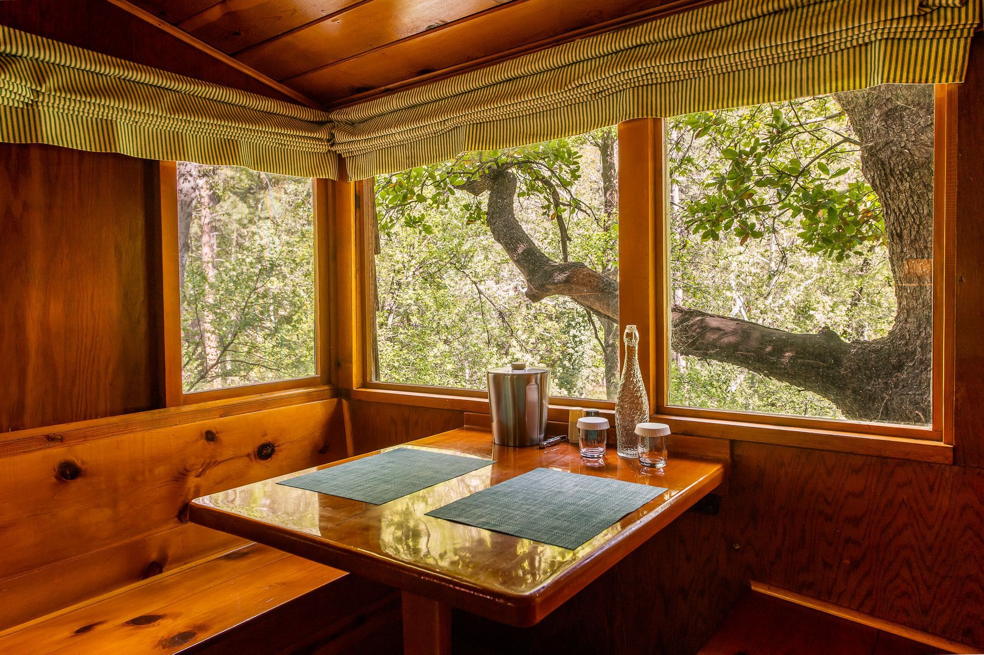 Cozy wooden booth with a table set for two, overlooking a green forest view.
