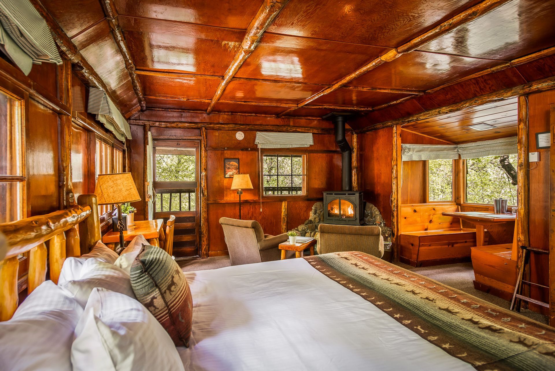 Cozy wooden cabin bedroom with a fireplace, large bed, and outdoor views.