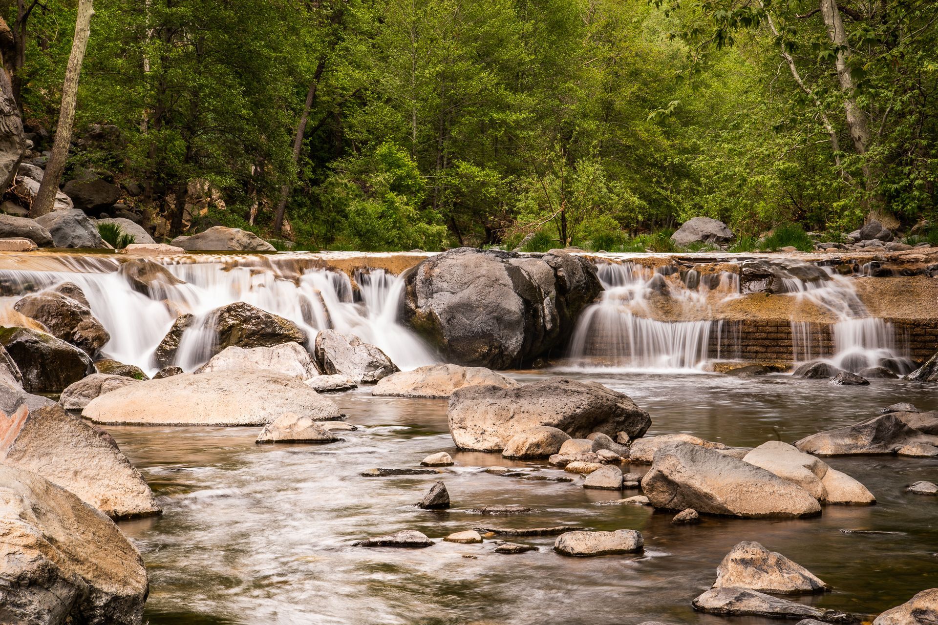 Waterfall cascading over rocks, surrounded by trees, in a river setting.