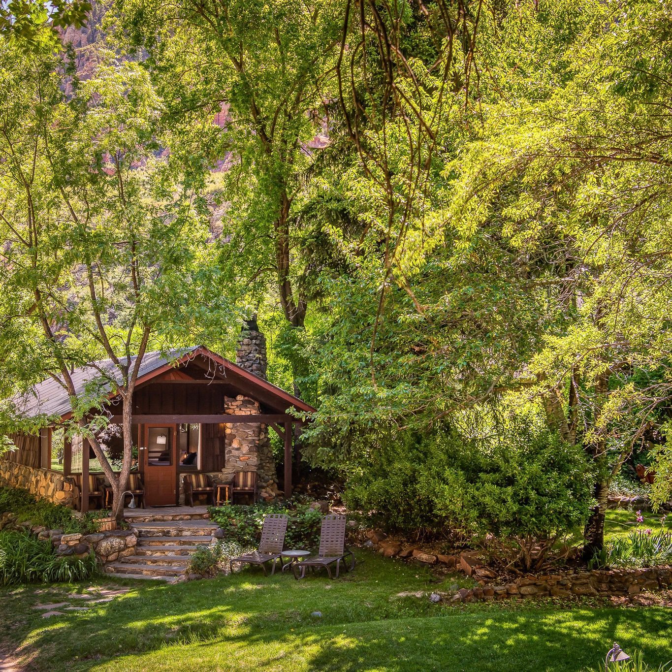 A small cabin made of stone is surrounded by trees and greenery on a bright sunny day.