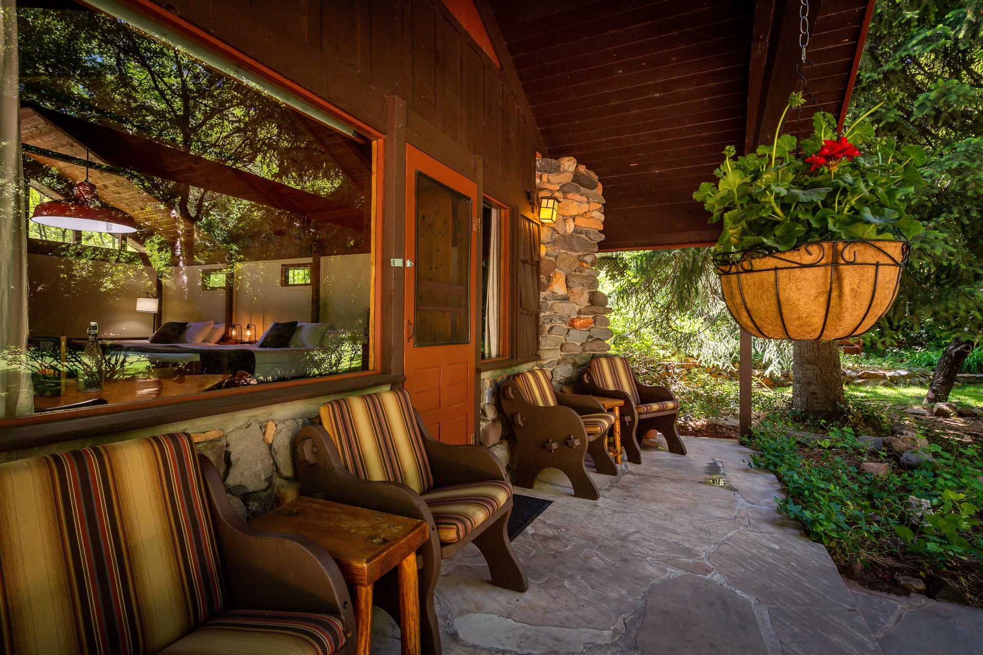 Covered porch with wooden chairs, a stone wall, and a hanging basket of flowers.