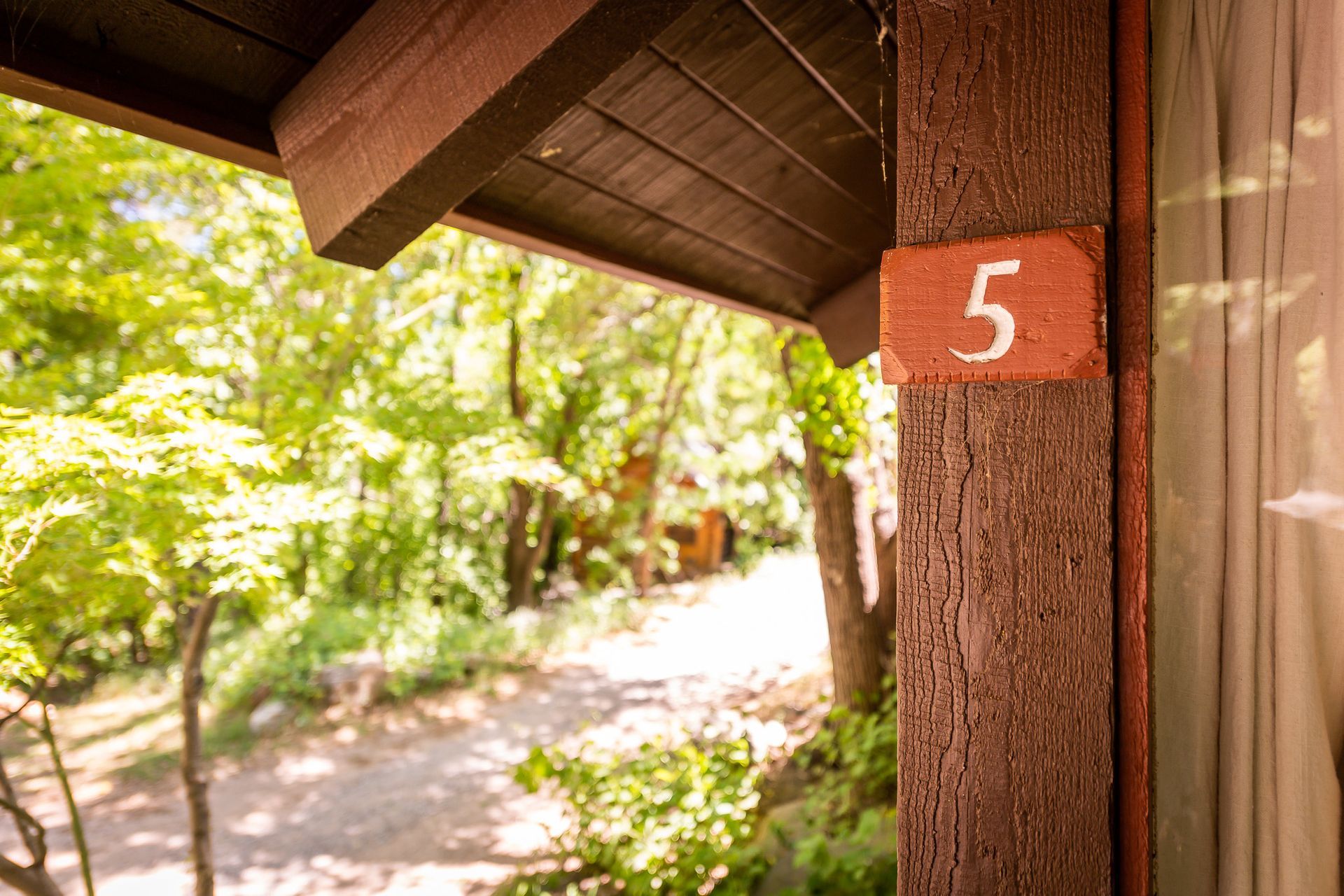 Number 5 on a wooden post under a porch roof, with a blurred forest path in the background.
