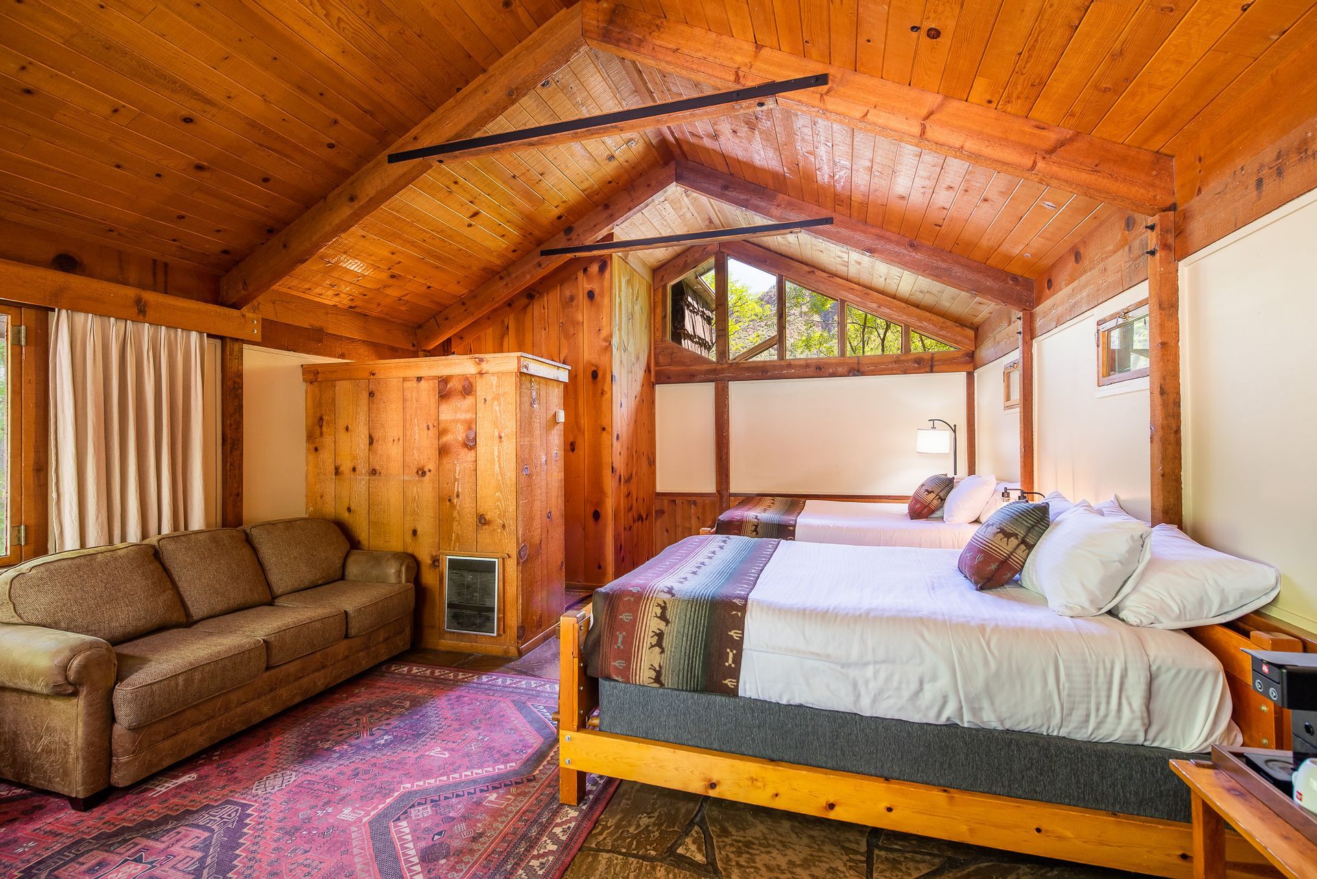 Cozy cabin bedroom with two beds, a sofa, and wood paneling.