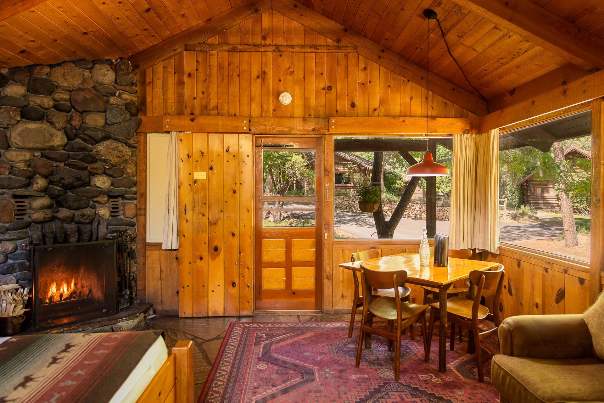 Cozy cabin interior with fireplace, wooden walls, dining table, and large windows.