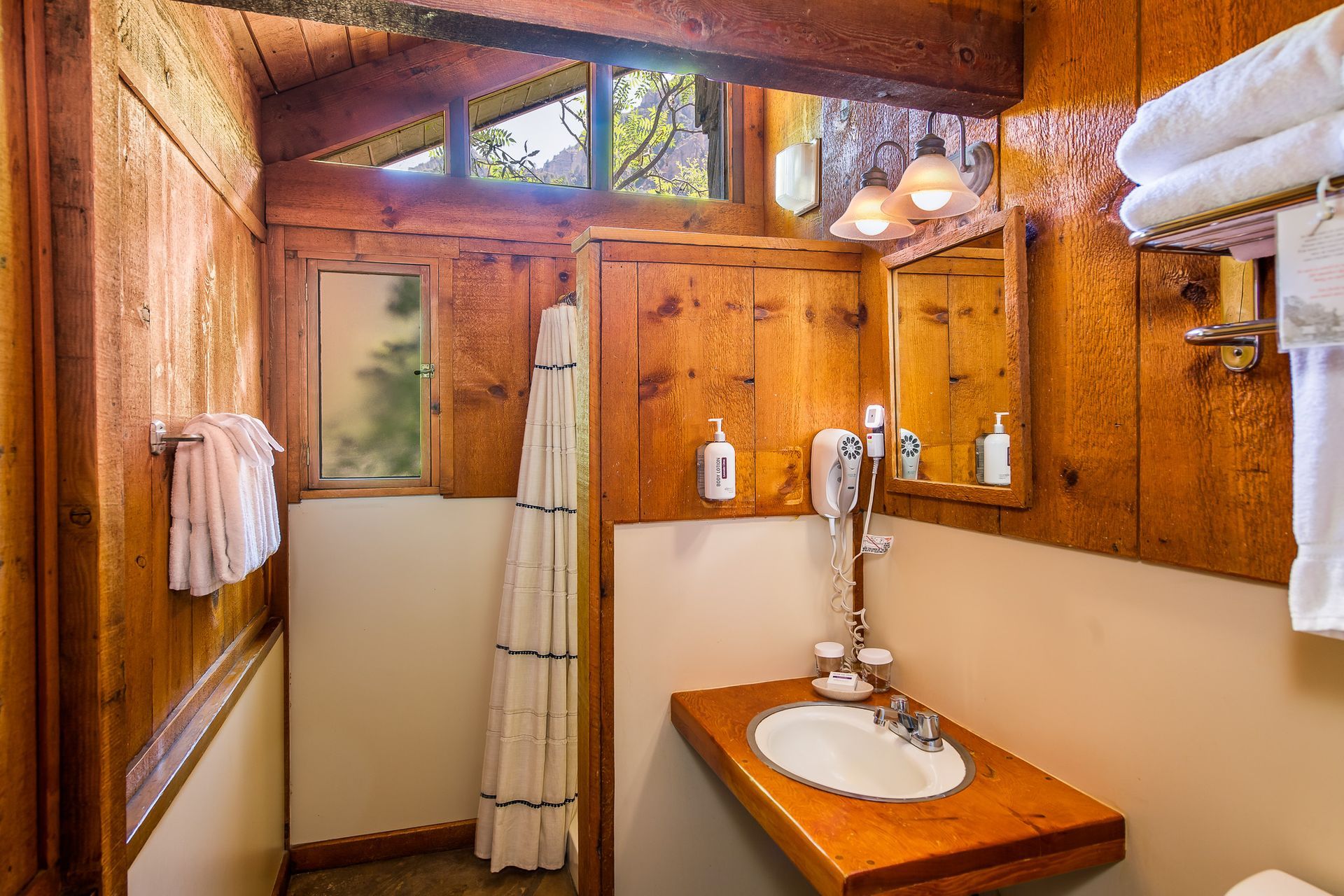 Bathroom with wood paneling, small window, sink, mirror, towels.