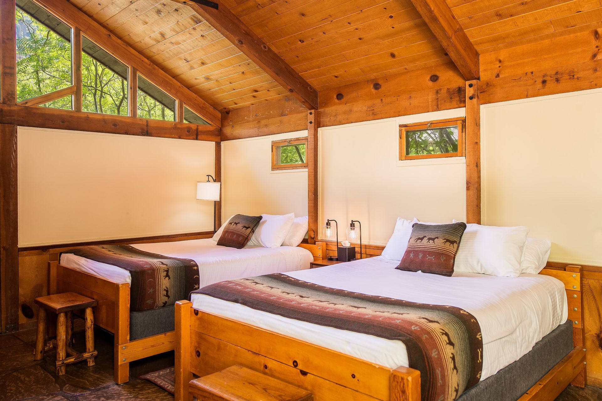 Two beds in a cabin with wood paneling, windows, and white walls.