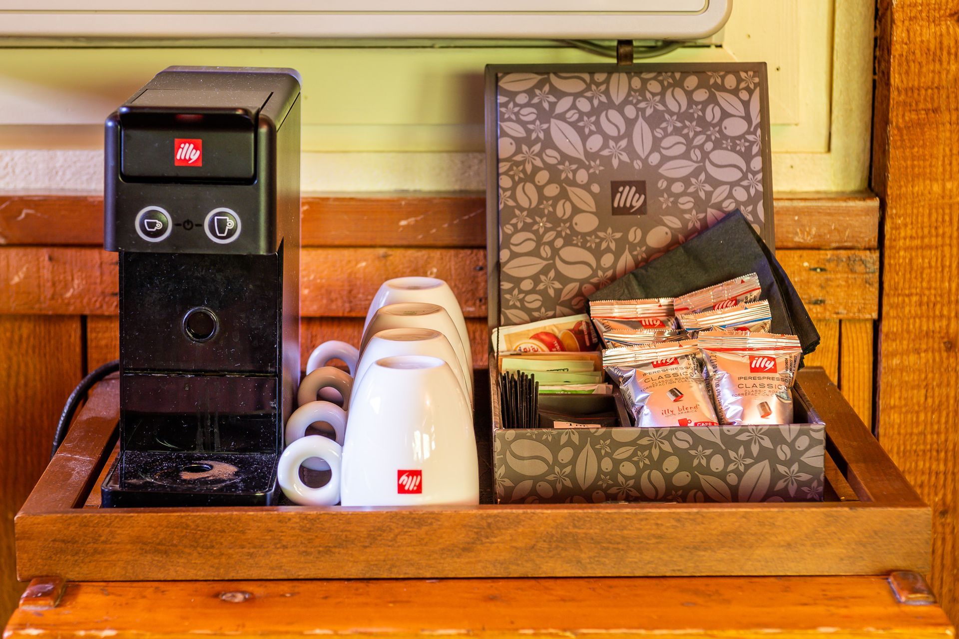 Coffee station with Illy espresso machine, cups, and a box of coffee and tea.