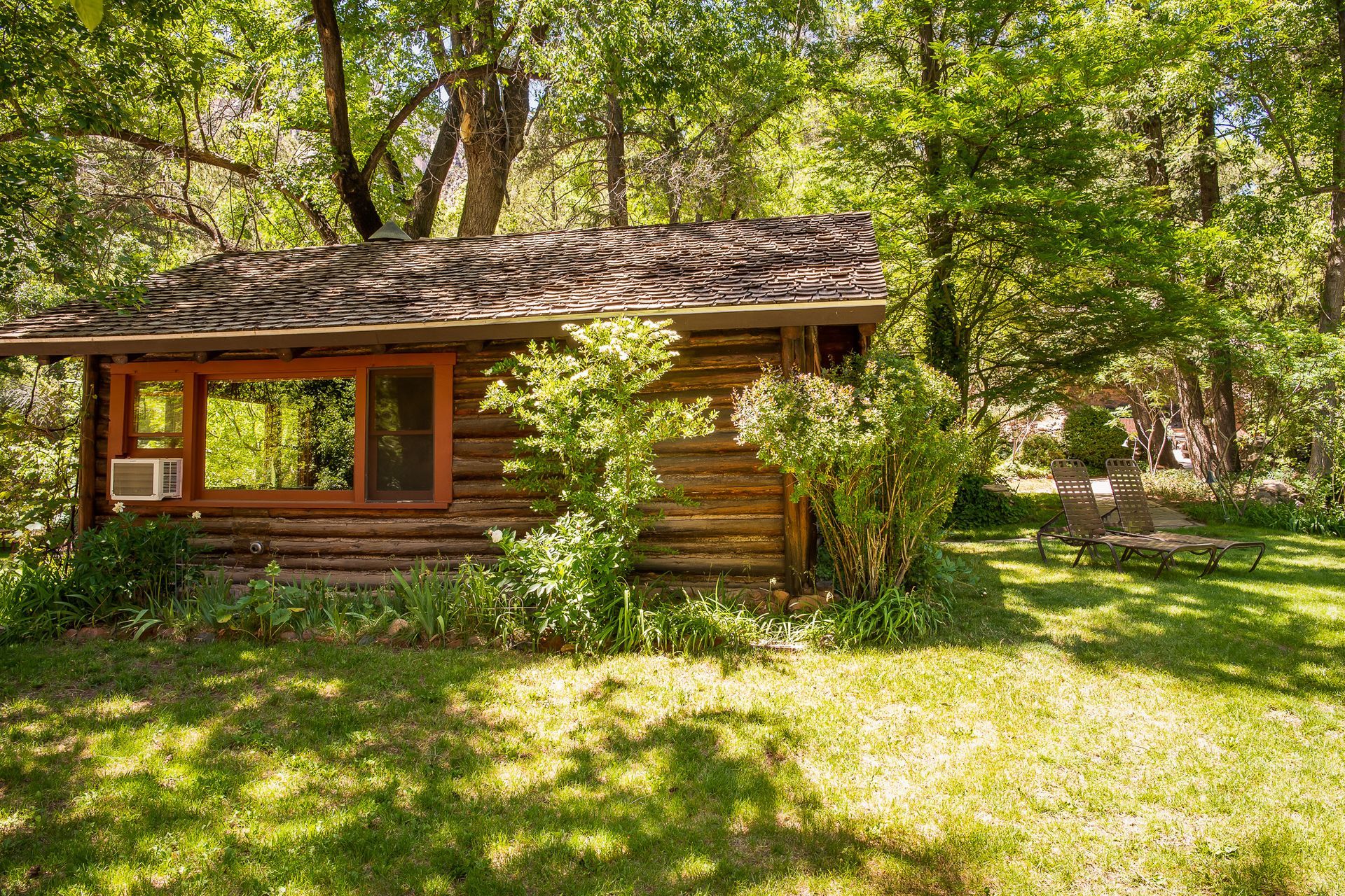 Log cabin nestled in a lush green forest, featuring a window and an air conditioner.