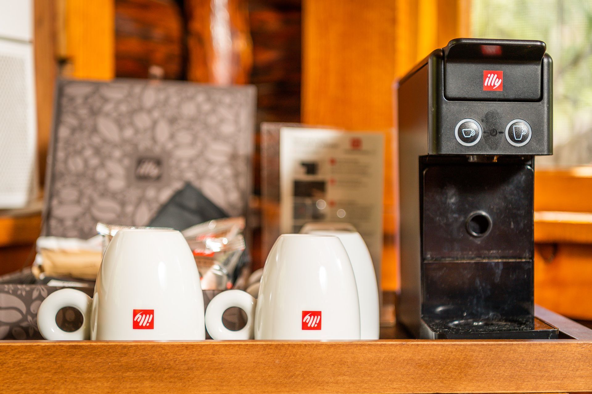 Coffee station with Illy machine, white mugs, coffee pods, and a brown wooden surface.