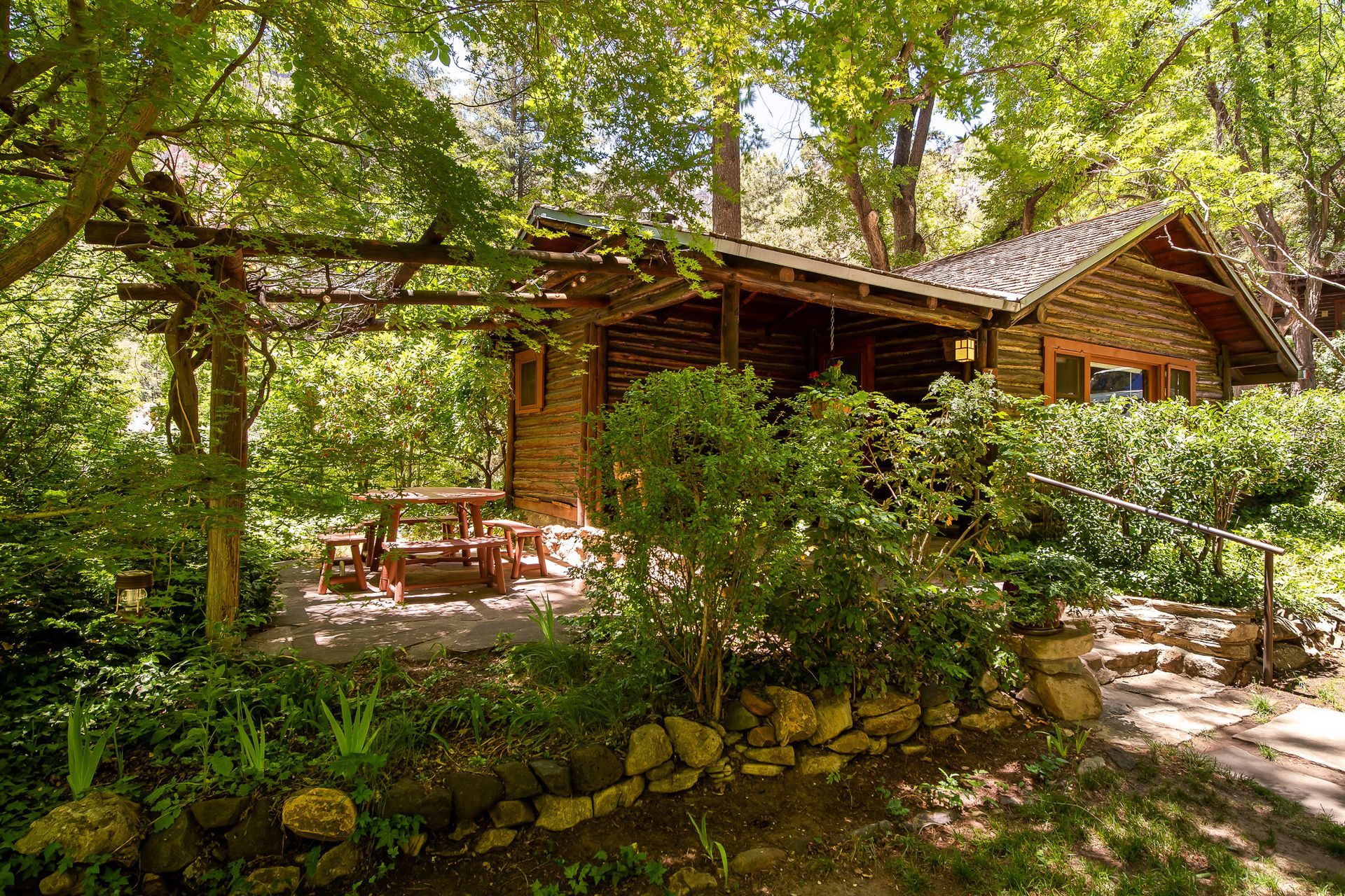 Rustic cabin with wooden walls and a shaded patio; outdoor dining set.