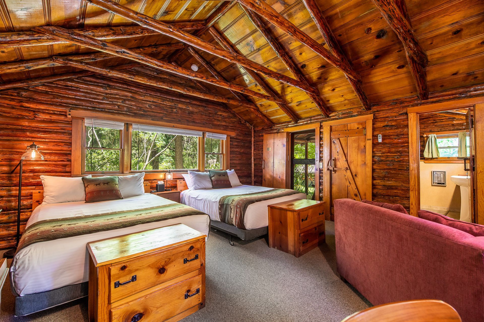 Cozy rustic cabin bedroom with two beds, wood furnishings, and a red couch.