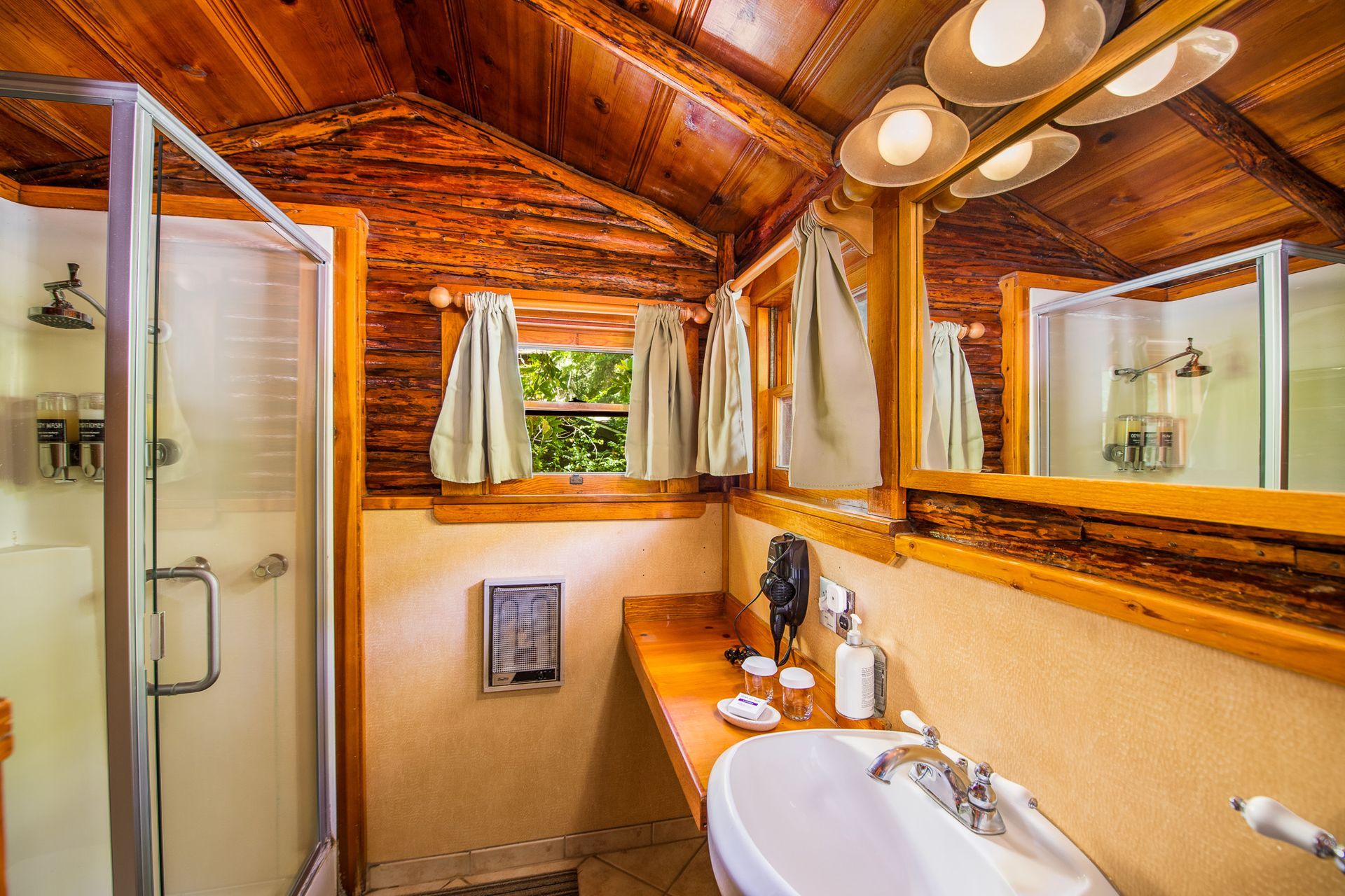 Rustic bathroom with wood ceiling, a shower, a vanity with sink, mirror, and small window.