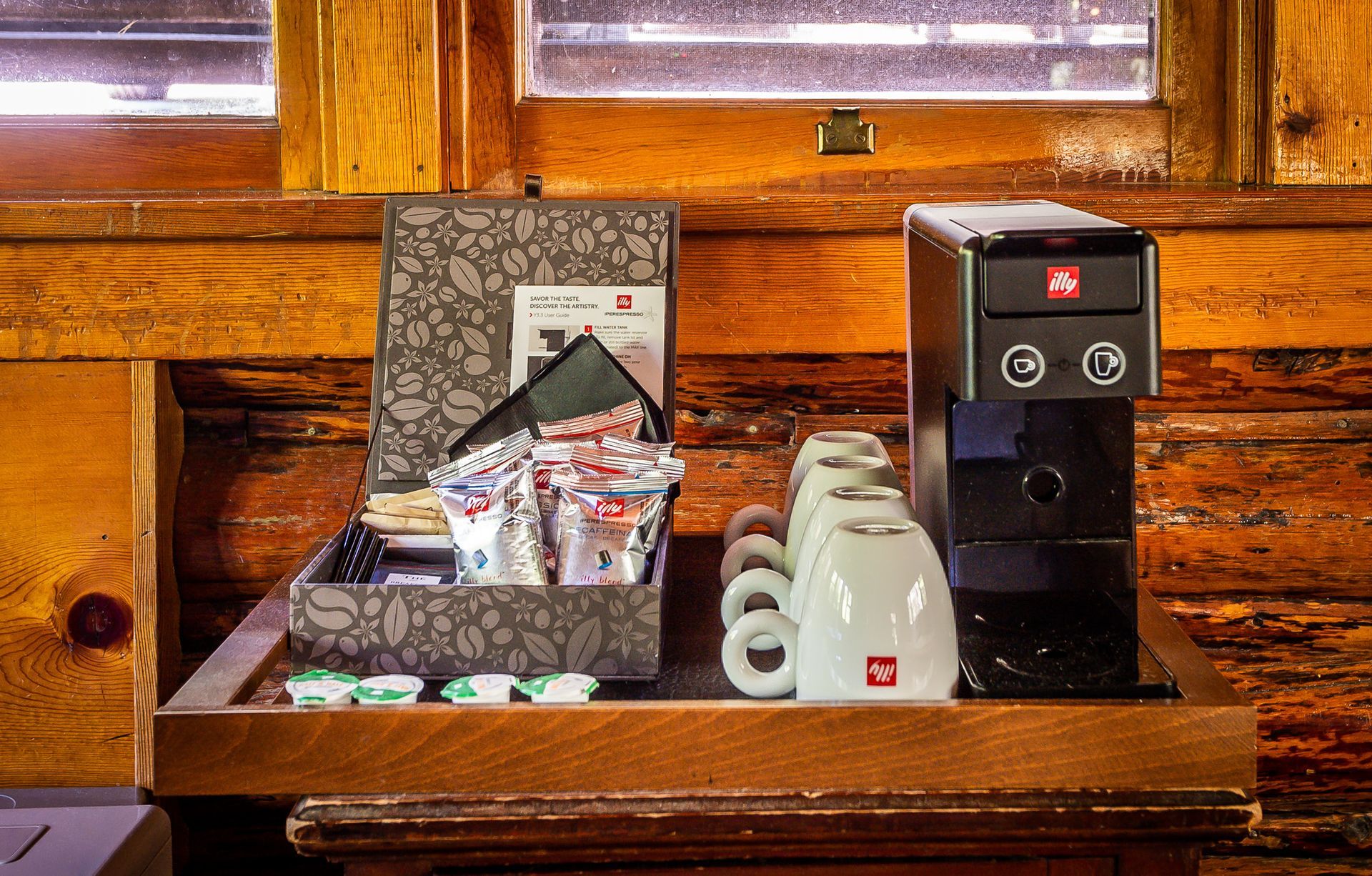 Coffee station on wooden surface with espresso machine, cups, and condiments.