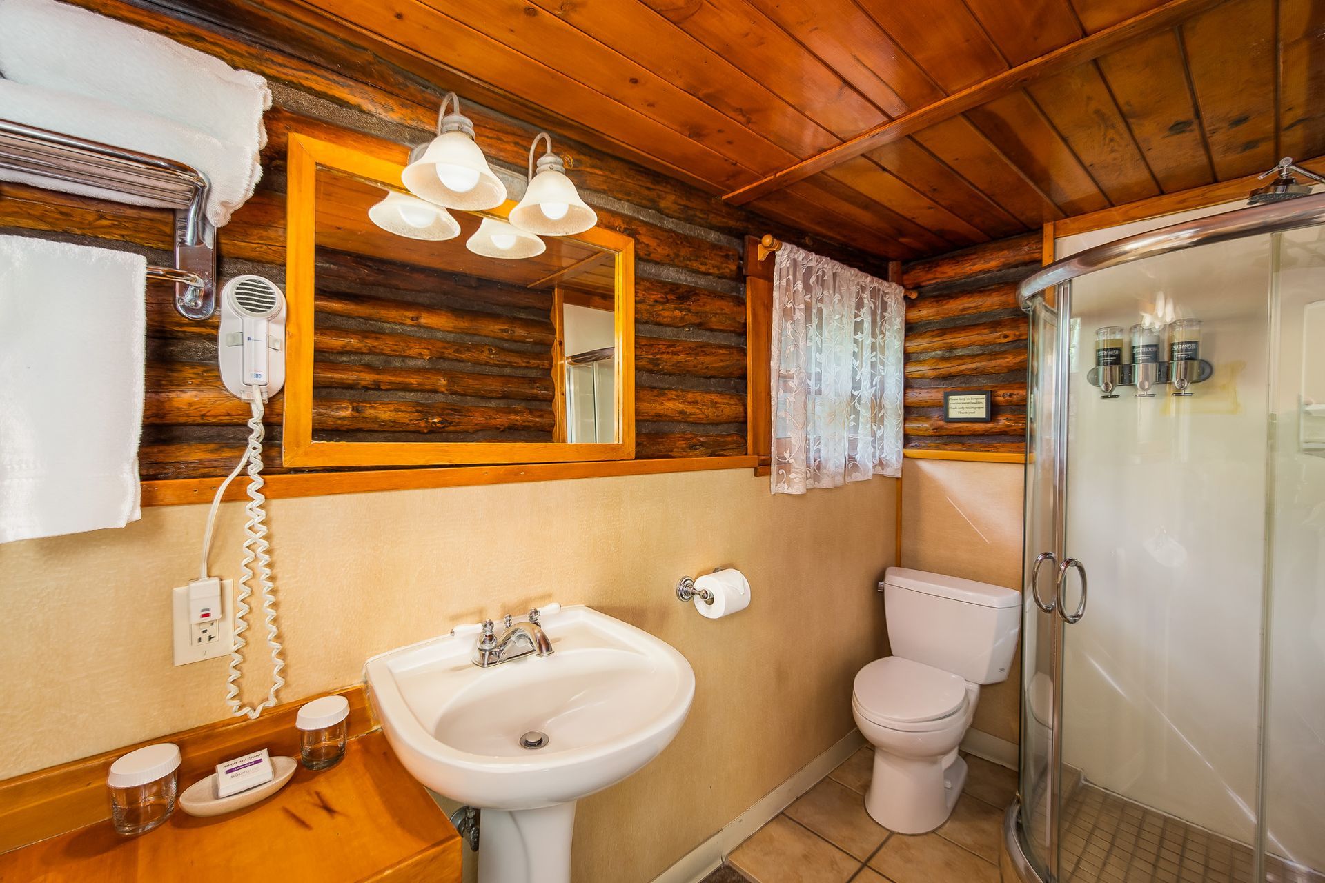 Rustic bathroom with wooden walls and ceiling, pedestal sink, and glass shower.