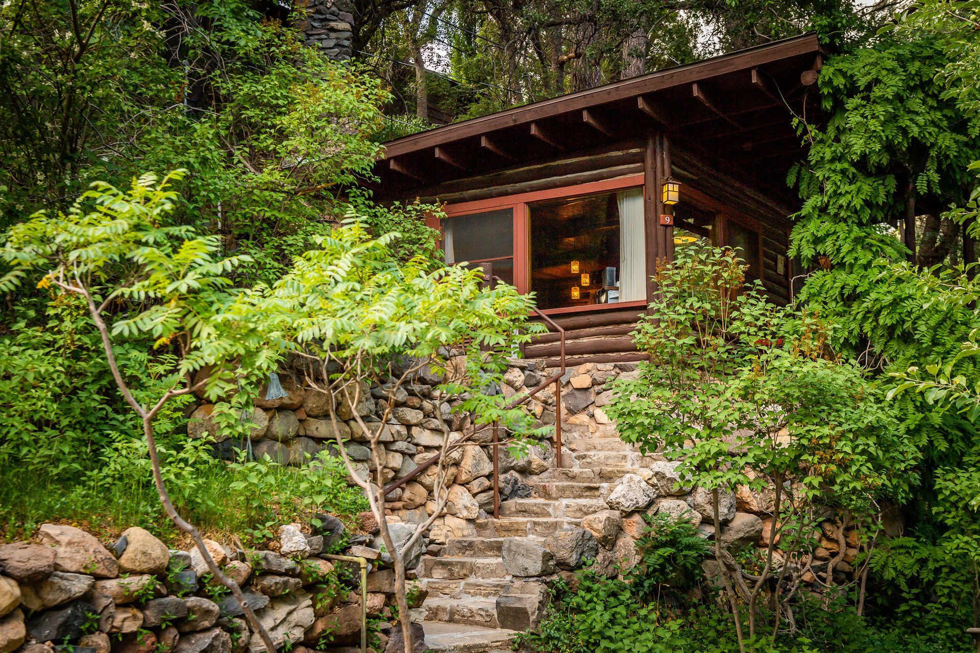 Cabin nestled in lush green foliage, accessible via stone steps.