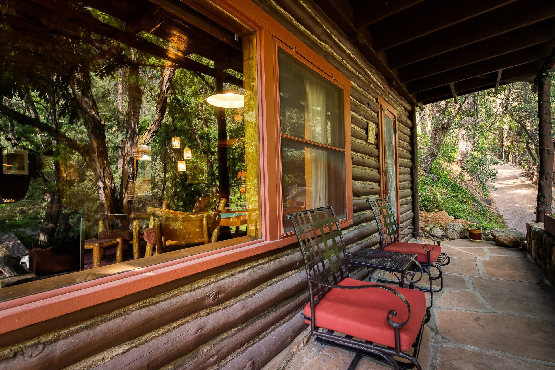 Log cabin porch with red cushioned chairs; window reflects the interior and trees.
