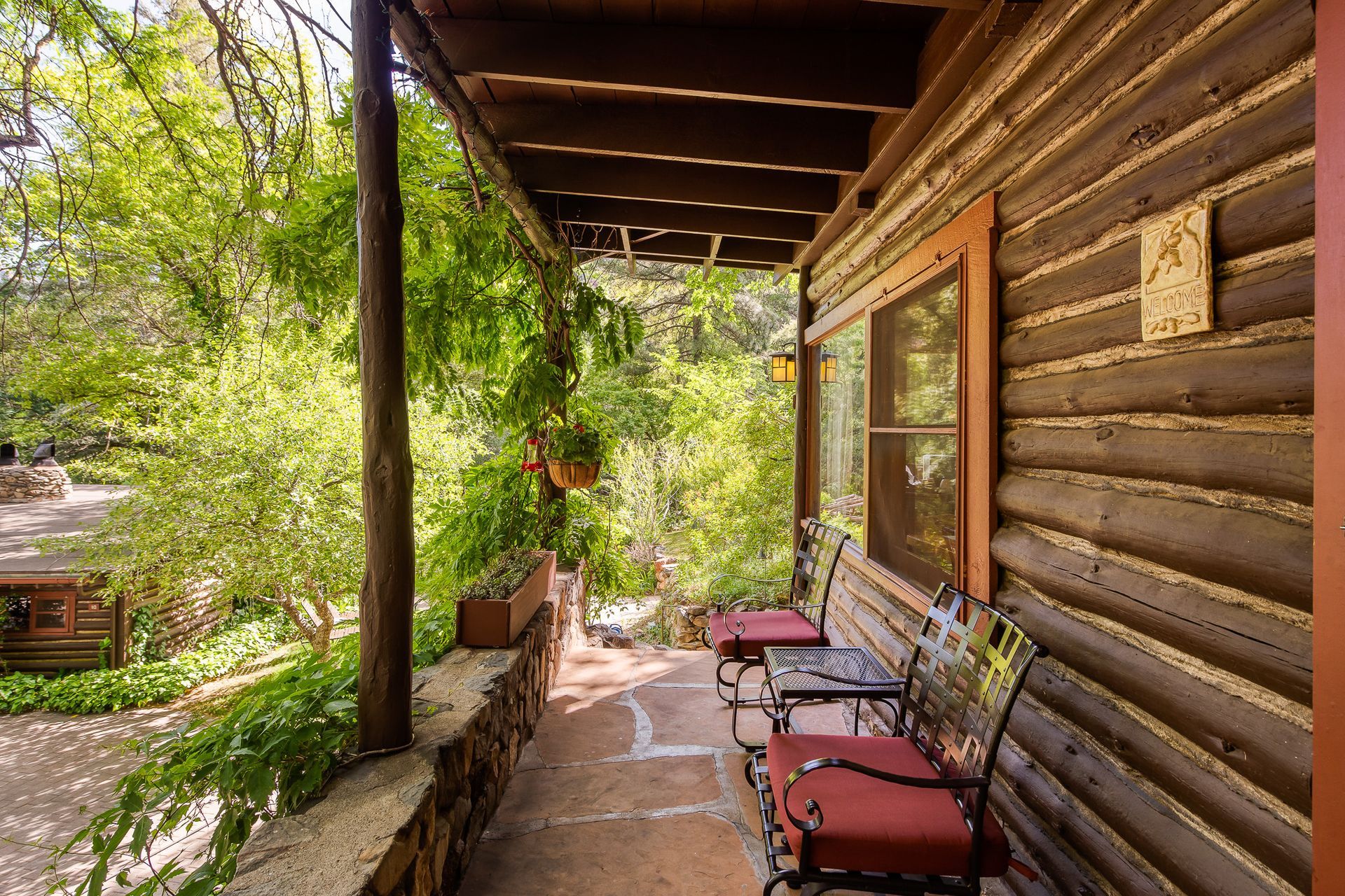 Log cabin porch with red cushioned chairs, overlooking lush greenery.