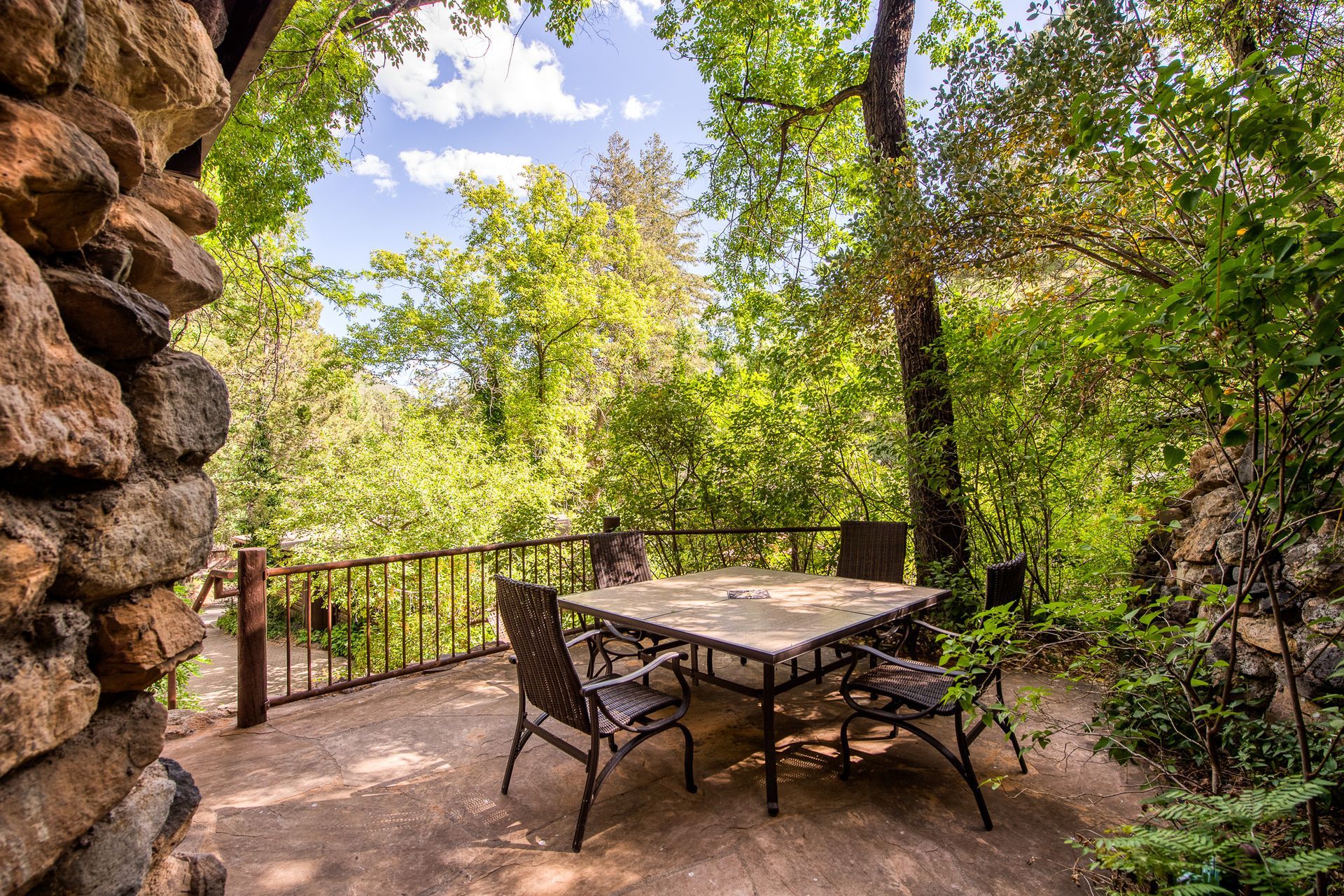 Stone patio with table and chairs overlooking lush greenery.