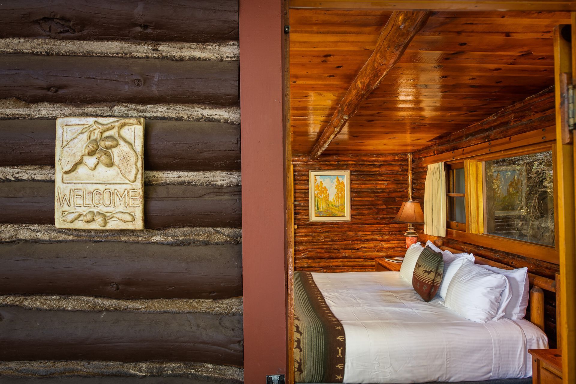 Log cabin interior with a bed, welcome sign, and wooden walls.