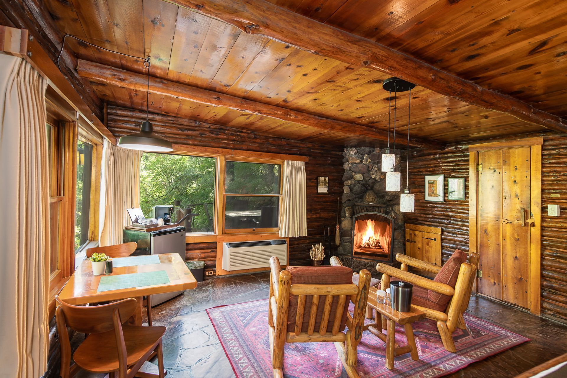 Cozy cabin interior with wood beams, fireplace, and rustic furniture. Natural light streams through windows.