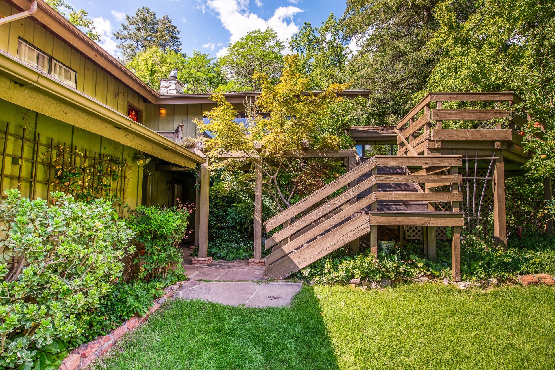 Exterior of a house with wooden deck and stairs amidst green foliage.