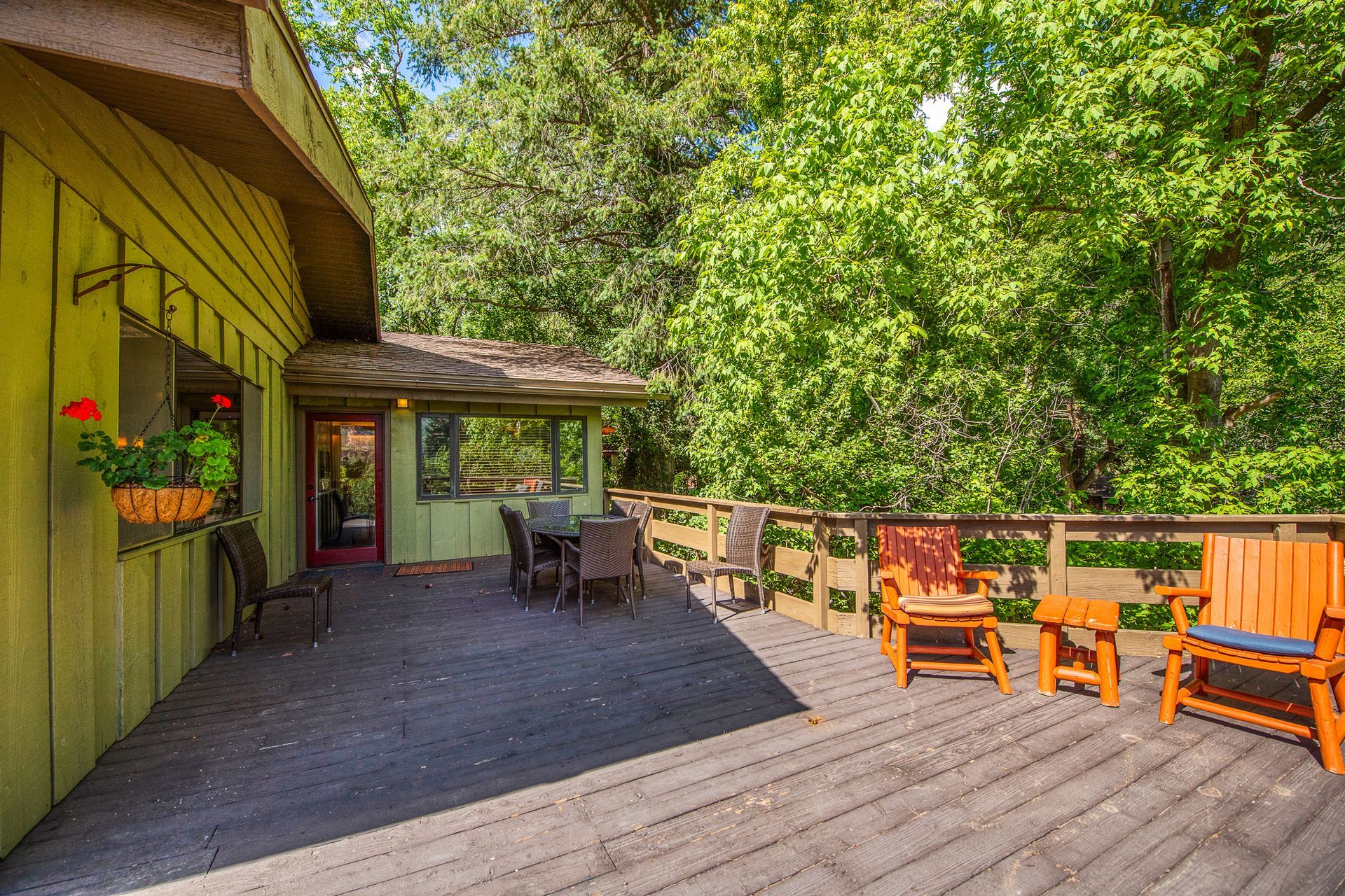 Wooden deck with outdoor furniture, overlooking lush green trees.