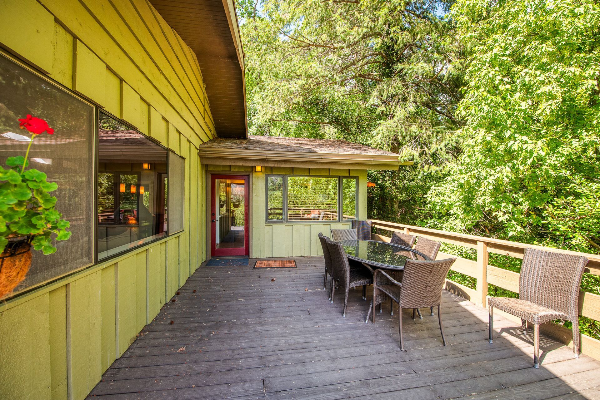 Deck with table and chairs, overlooking a lush green forest. Building is yellow.