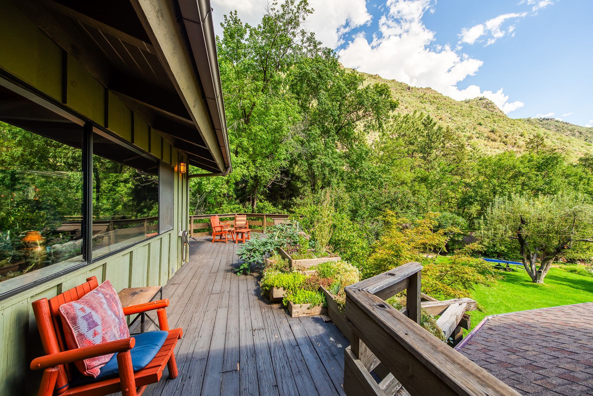 Wooden deck with orange chair, overlooking green trees, garden and a mountain.