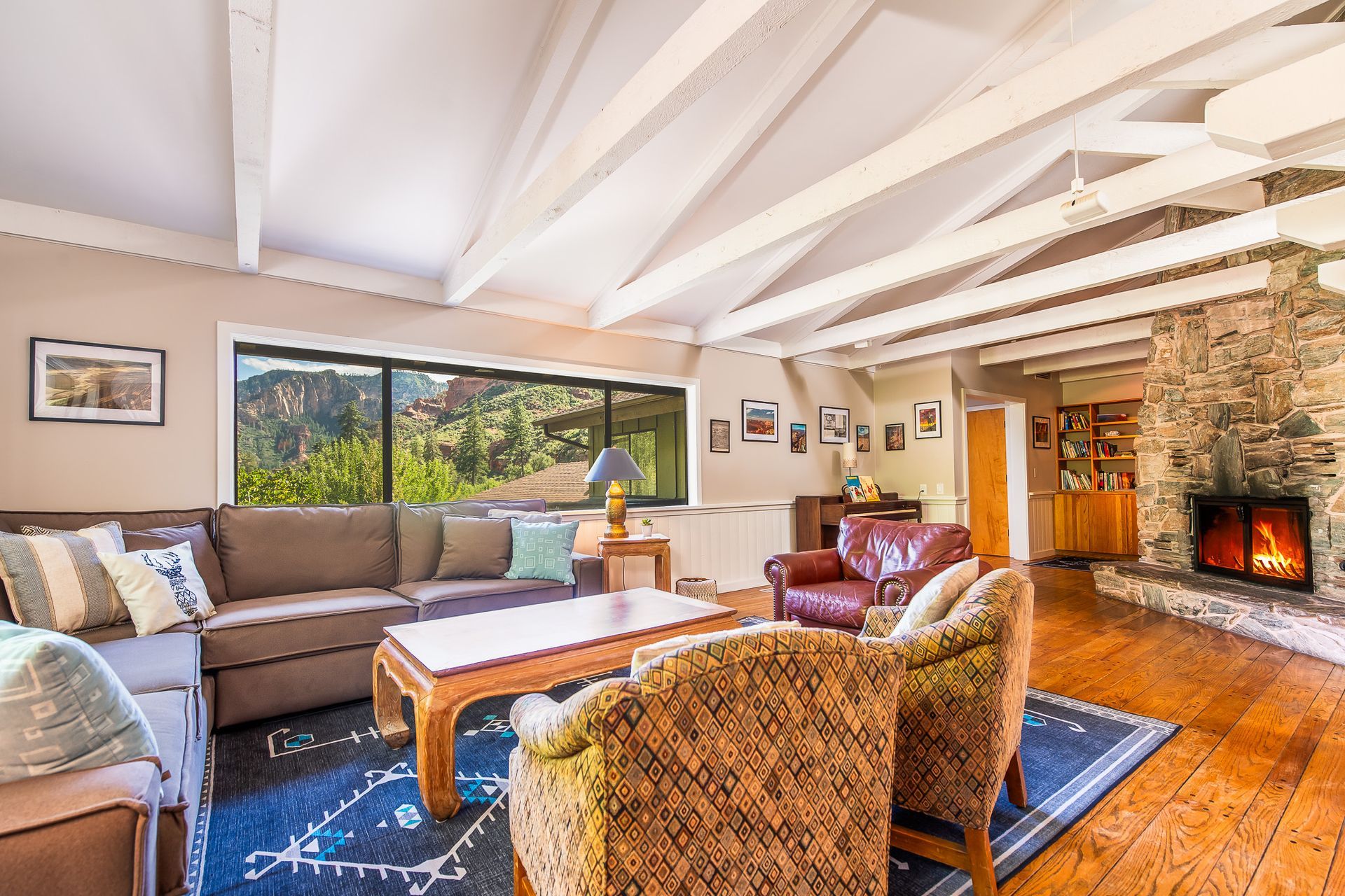 Living room with stone fireplace, exposed beams, brown sectional sofa, and mountain view.