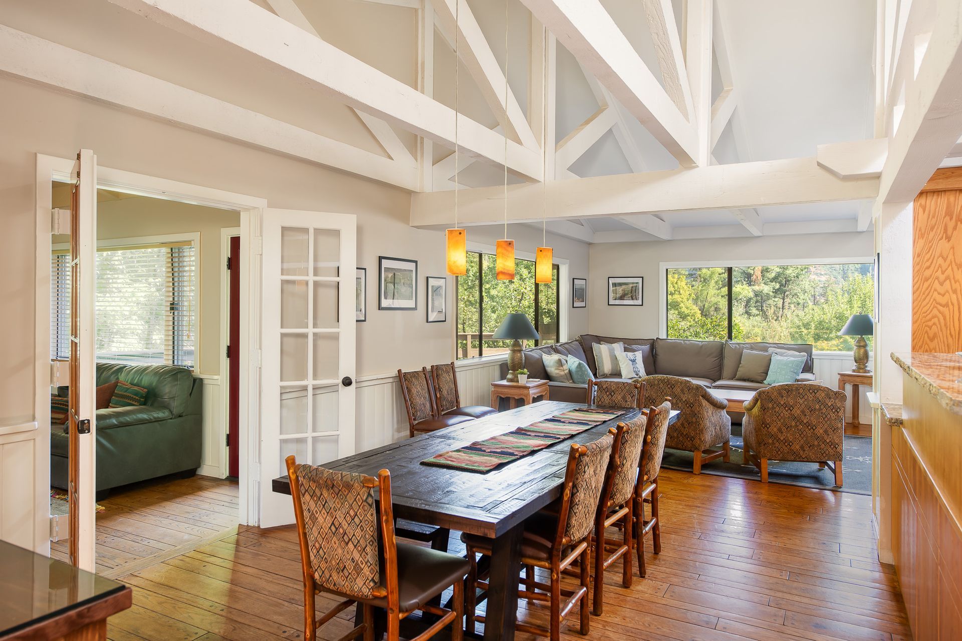 Dining area with long dark table and woven chairs, open to a living room with a large sectional sofa.