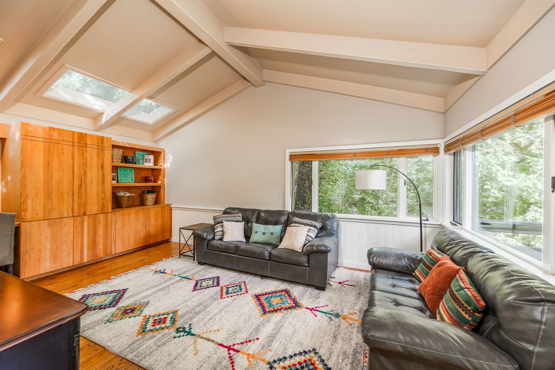 Living room with a gray sofa, rug with colorful designs, skylights, and wooden storage.