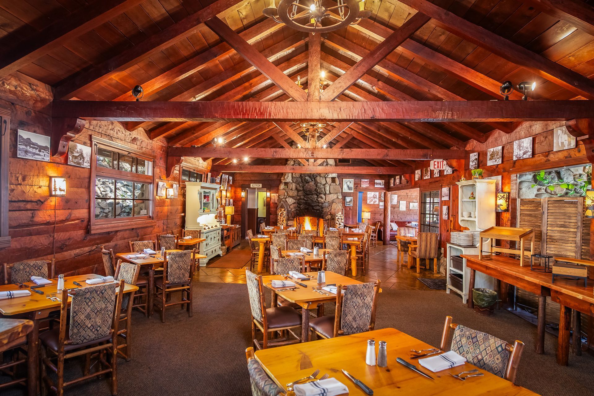 Rustic restaurant interior with wooden beams, tables, fireplace, and stone walls.