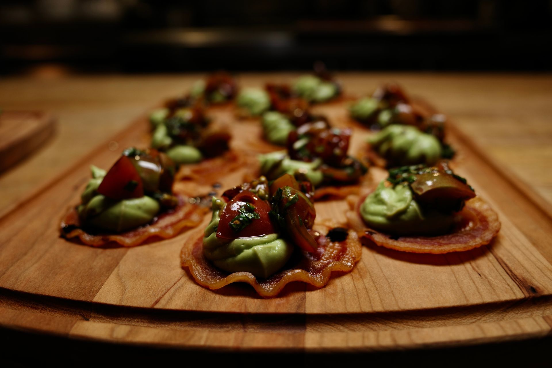 Appetizers: Crispy bacon rounds topped with avocado, tomatoes, and herbs, arranged on a wooden platter.