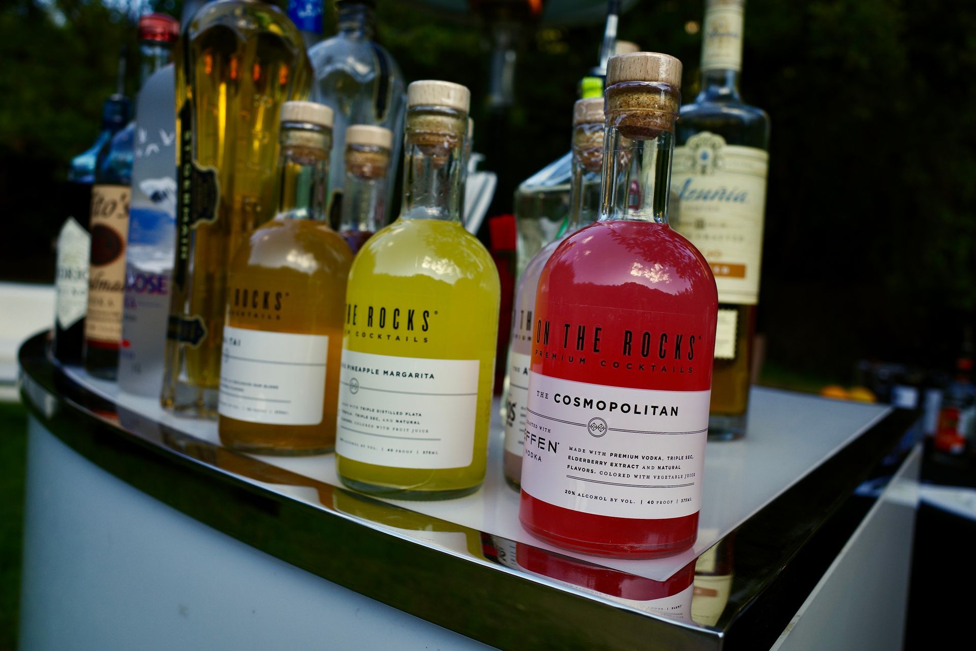 Bottles of various cocktails, including a pink Cosmopolitan, on a bar.
