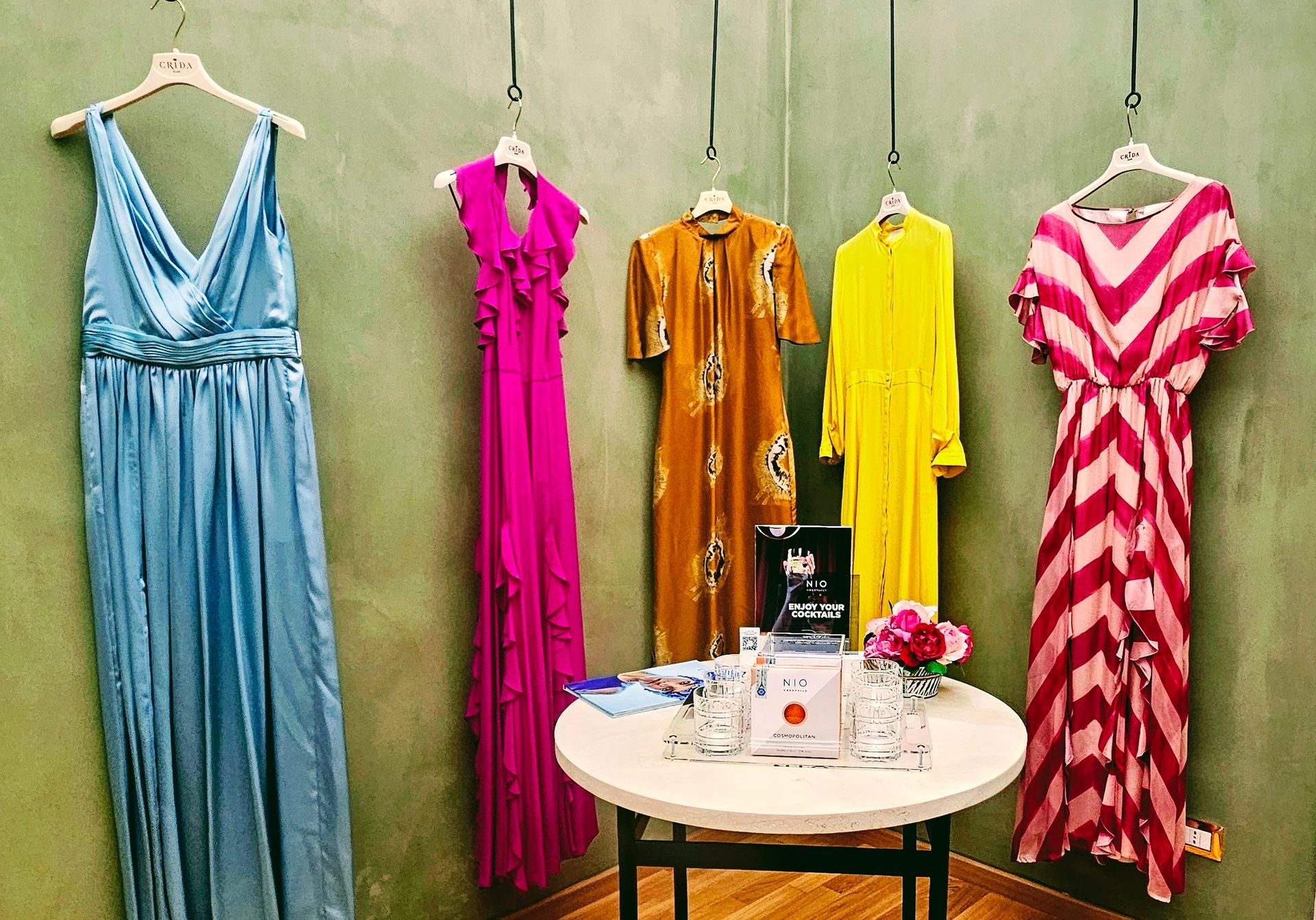 A row of designer Italian gowns hanging on a wall next to a table.