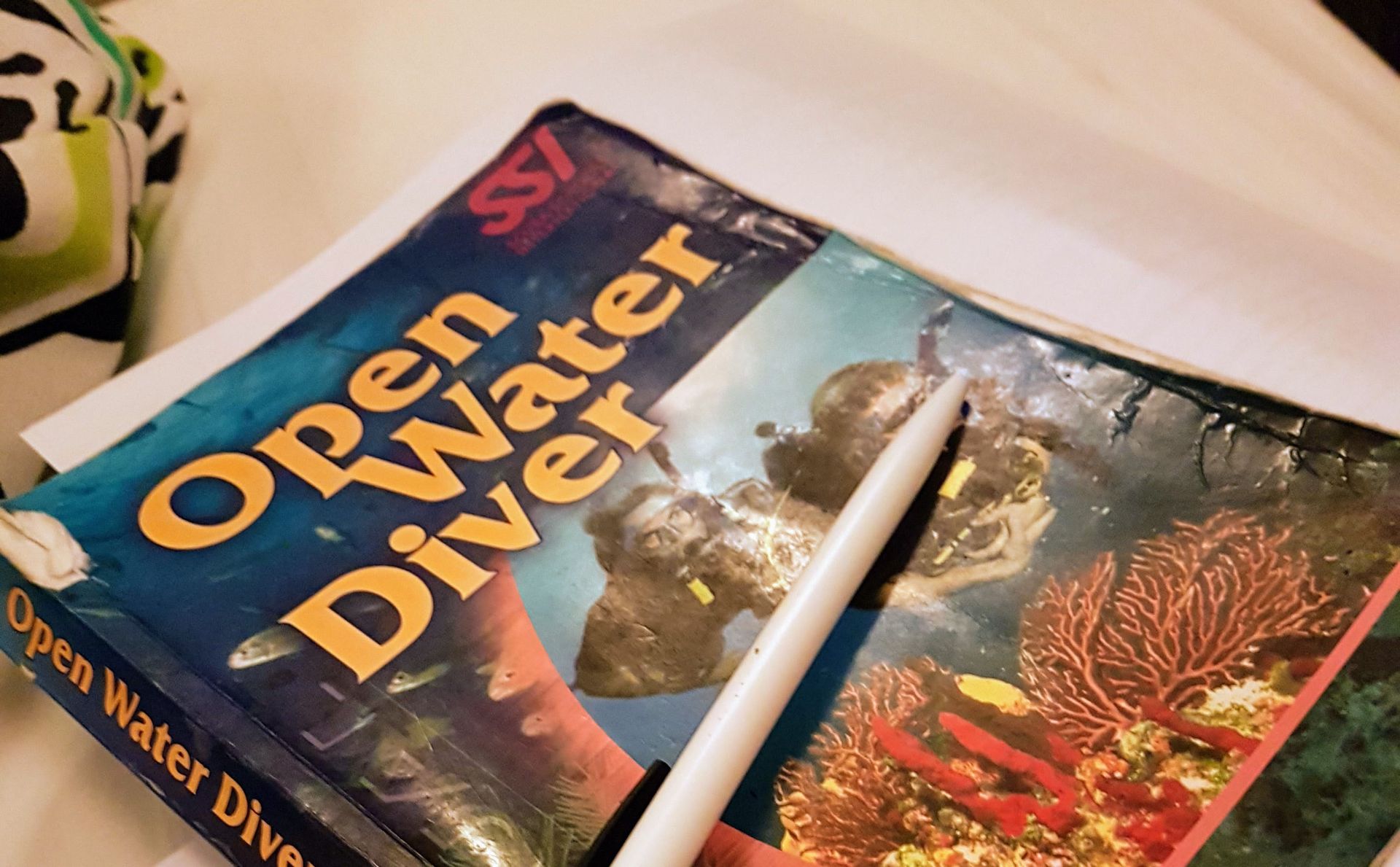 A book titled SSI open water diver sits on a table next to a pen