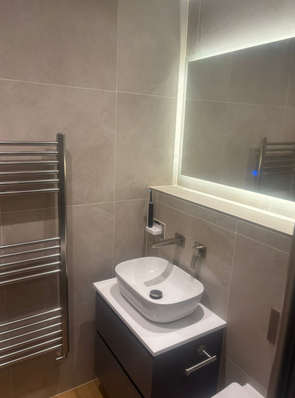 Modern bathroom with a vessel sink, heated towel rack, and a mirror with LED lighting.