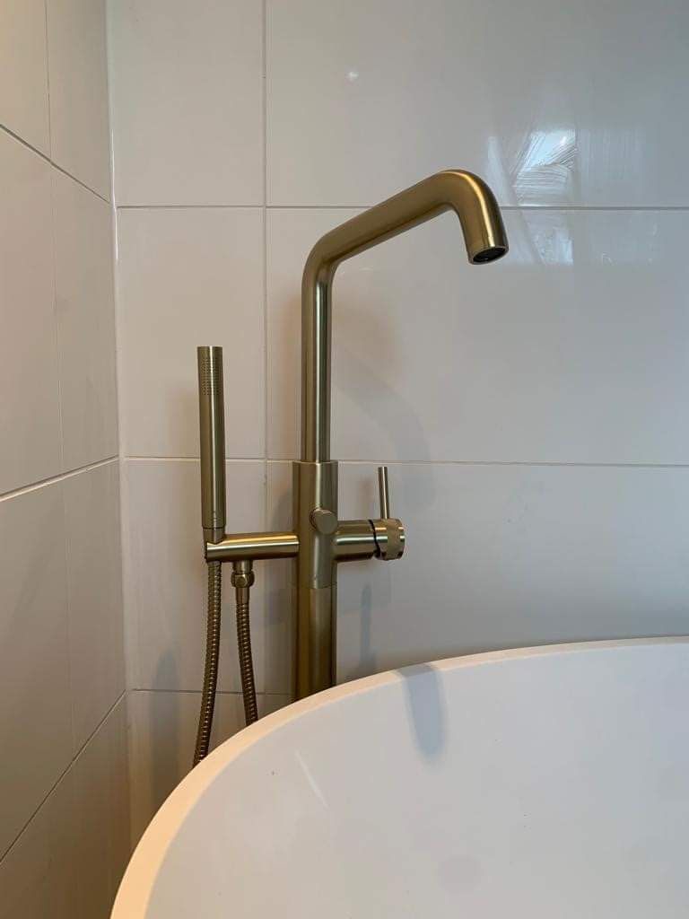 A bathtub with a gold mixer tap attached to it in a bathroom.