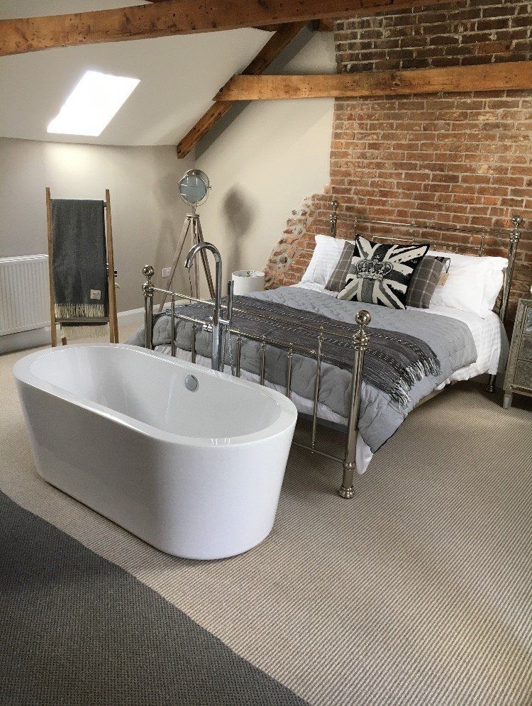 A bedroom with a bed , bathtub , mirror and brick wall.
